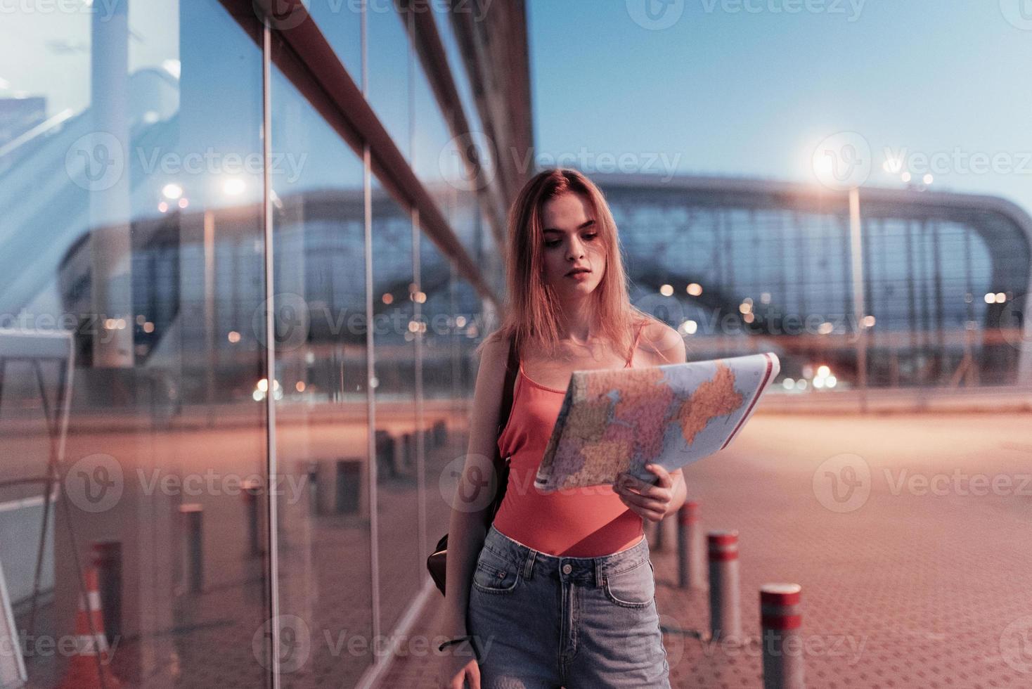 jeune fille séduisante regardant la carte dans sa main en marchant près du bâtiment de l'entreprise photo