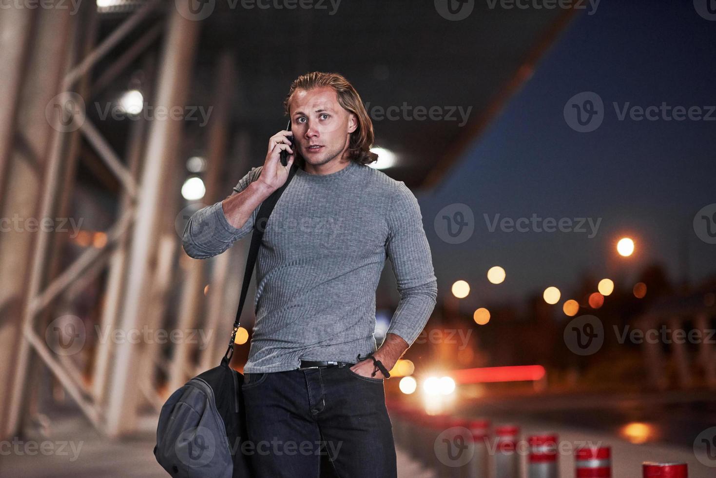 marcher dans la rue. homme aux cheveux longs et bagages de voyage attendant que le taxi vienne le chercher photo