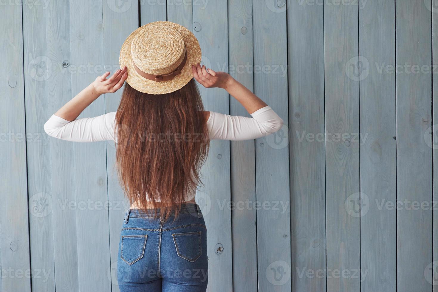 conception de style. fille au chapeau a tourné le dos à la caméra. debout sur le fond en bois photo