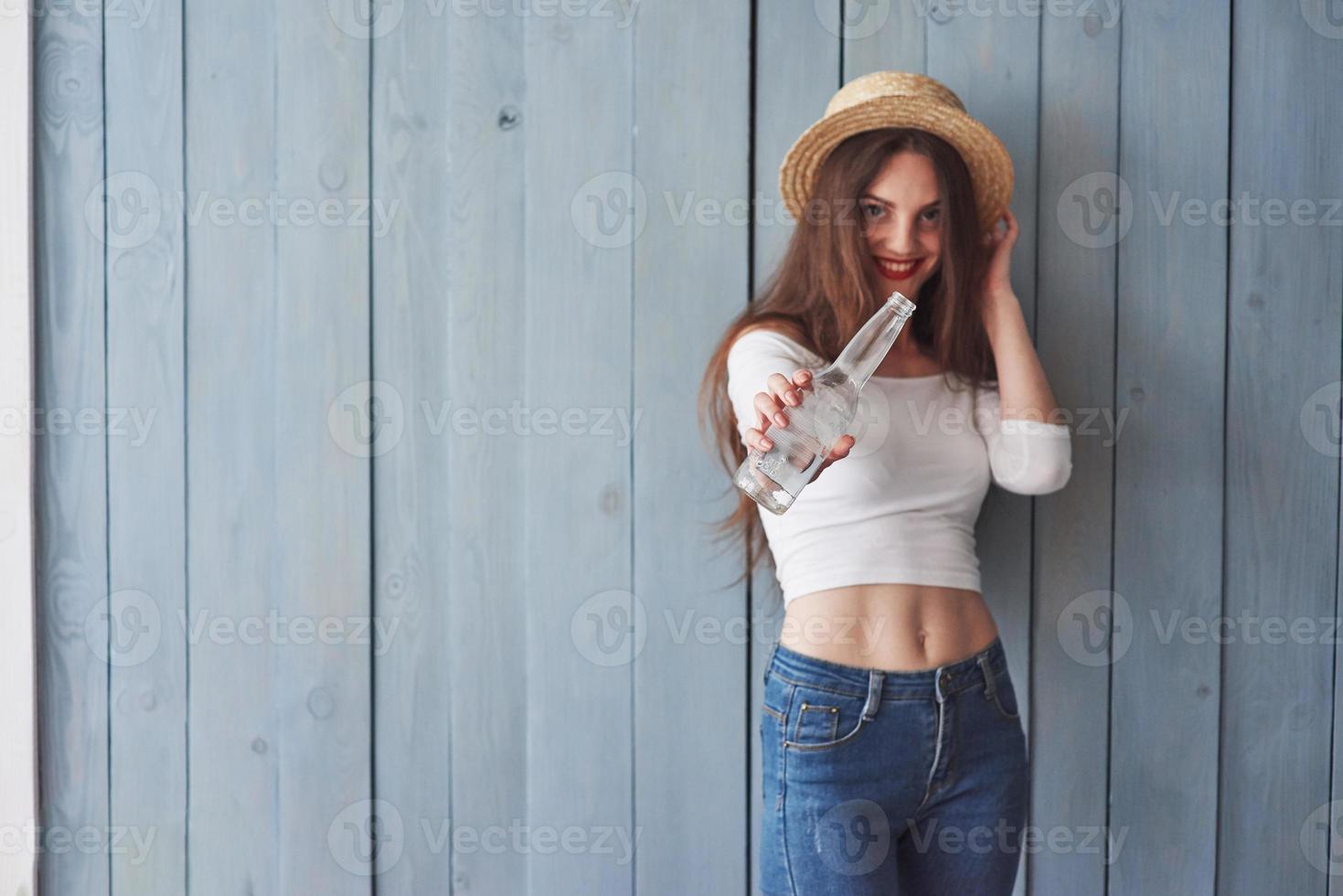 ne vois-tu pas que c'est vide. faire quelque chose à ce sujet. portrait de belle jeune fille avec un chapeau sur la tête et une bouteille à la main debout contre un mur en bois photo