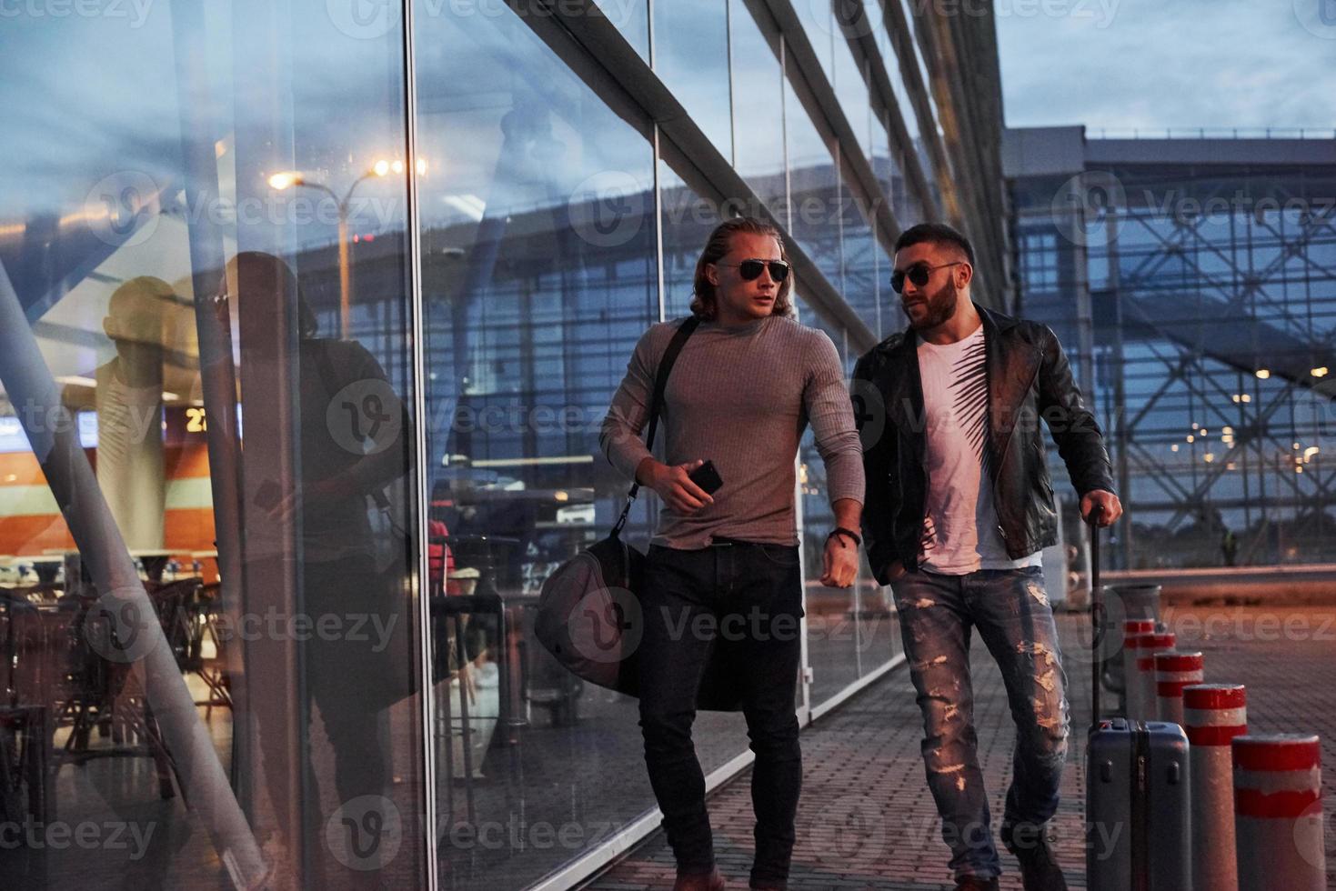 deux amis élégants portant des lunettes de soleil se sont rencontrés près du bâtiment du centre d'affaires et marchant devant la caméra photo