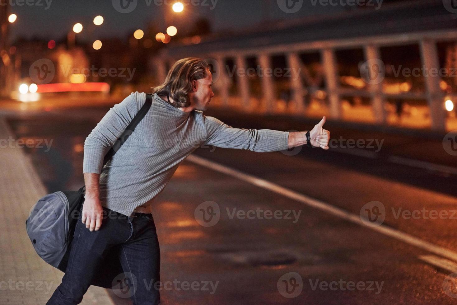 une sorte de voiture passe le long du chemin. jeune homme avec sac essayant d'arrêter la voiture parce qu'il est en retard photo