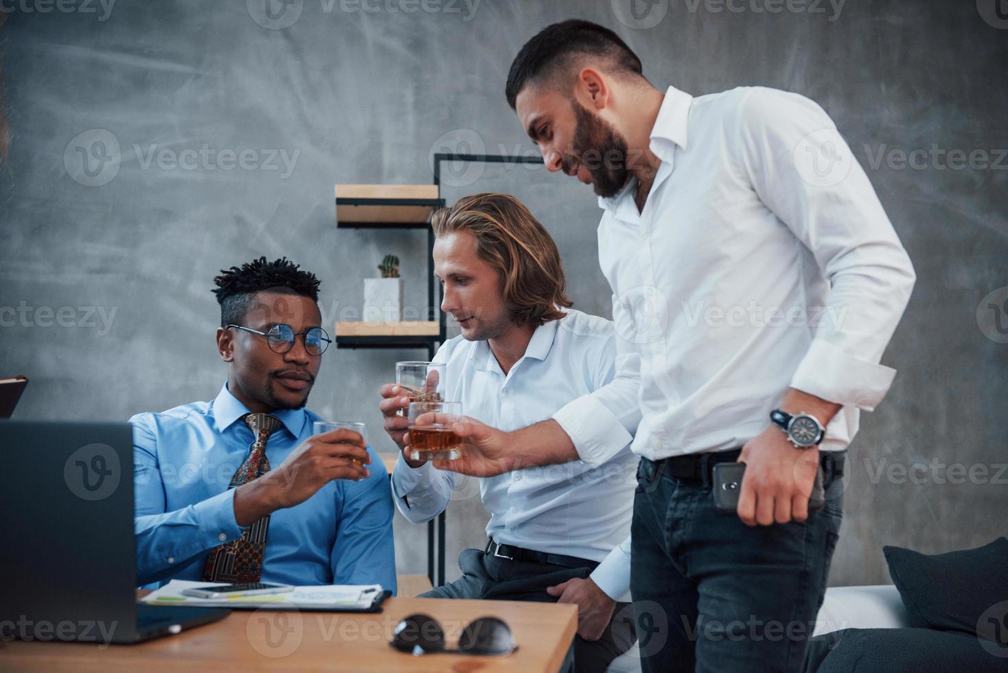 boire du whisky. groupe d'employés de bureau multiraciaux en vêtements formels parlant de tâches et de plans photo