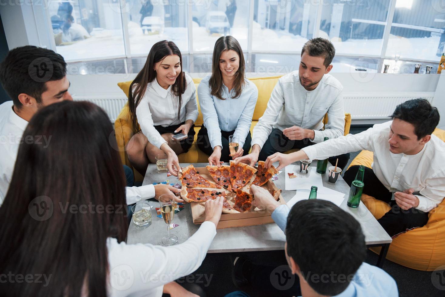 chacun a sa part. manger des pizzas. célébrant l'accord réussi. jeunes employés de bureau assis près de la table avec de l'alcool photo