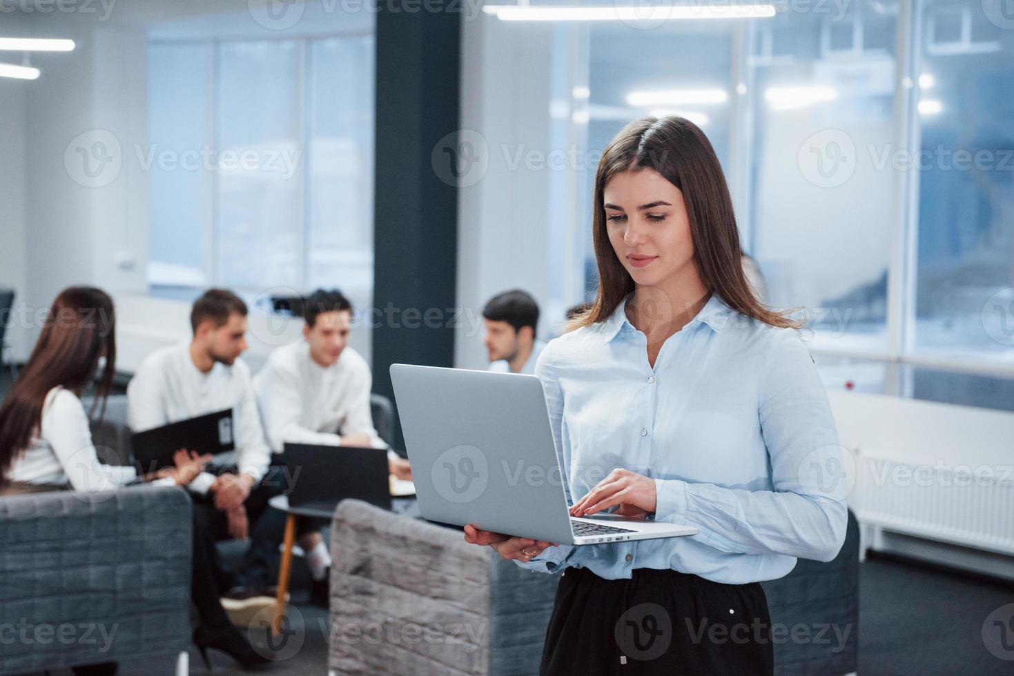 travailler avec un ordinateur portable. portrait de jeune fille se tient au bureau avec des employés en arrière-plan photo