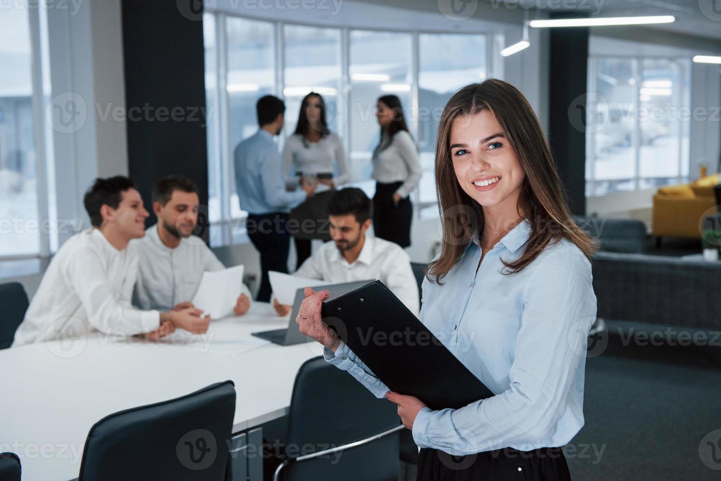 jeunesse réussie. portrait de jeune fille se tient au bureau avec des employés en arrière-plan photo