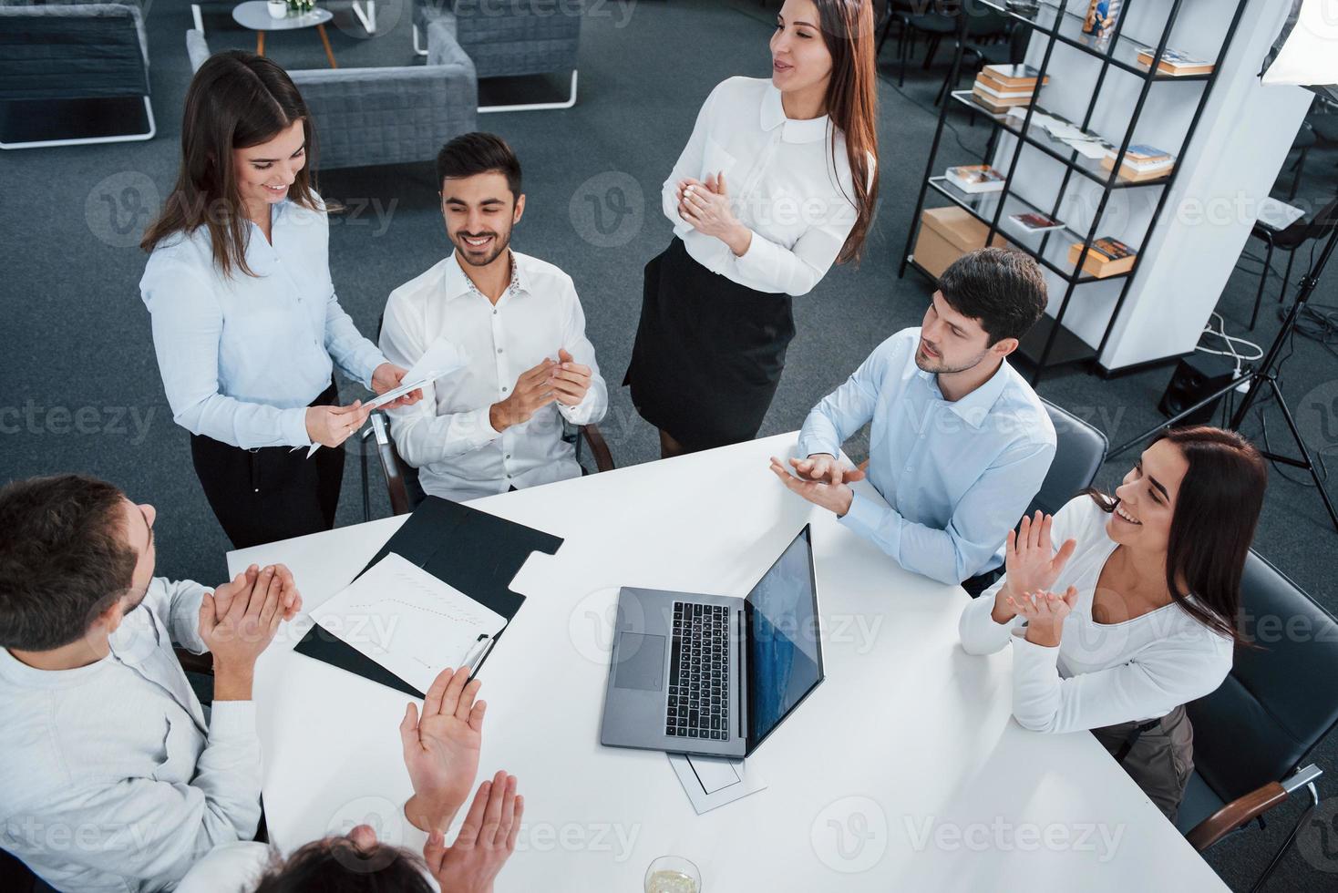 semble être une bonne nouvelle. vue de dessus des employés de bureau en tenue classique assis près de la table à l'aide d'un ordinateur portable et de documents photo