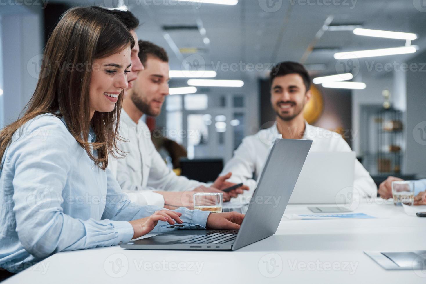 les gens ont une conversation d'affaires. vue latérale d'une fille travaille sur l'ordinateur portable de couleur argent au bureau et souriant photo