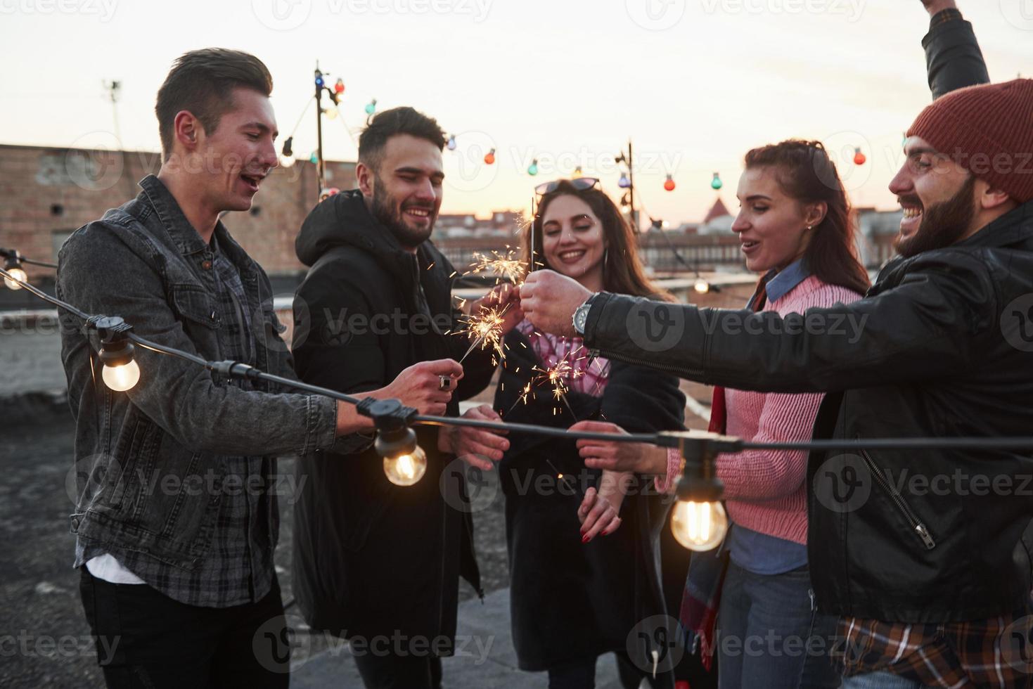 les vacances sont déjà venues pour ces gens. jouer avec des cierges magiques sur le toit. groupe de jeunes beaux amis photo