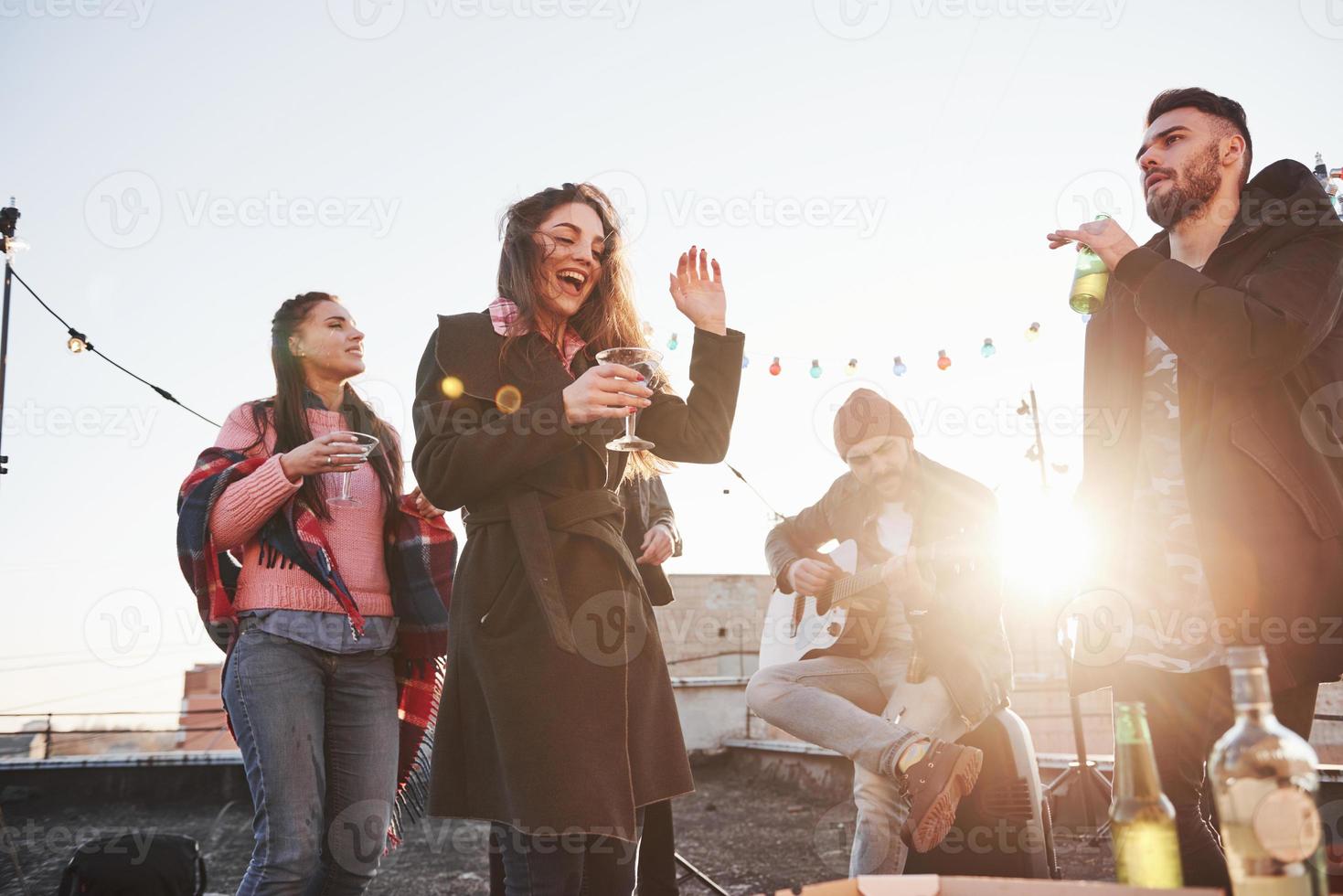 danser et chanter. fête sur le toit avec de l'alcool et du jeu de guitare. soleil derrière photo