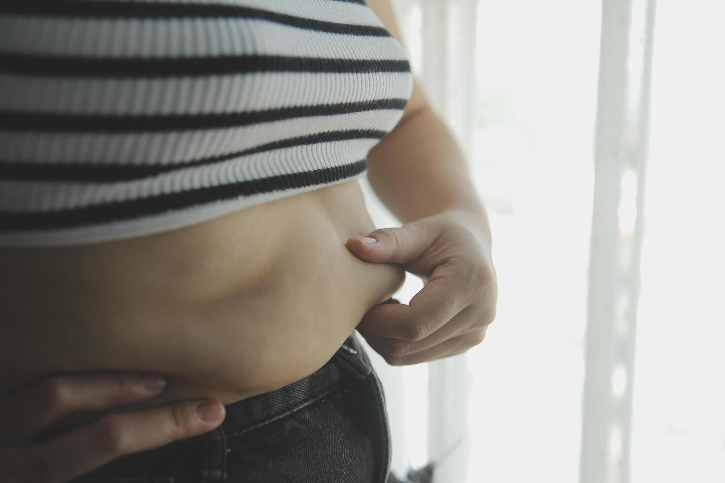 femmes corps graisse ventre. obèse femme main en portant excessif ventre graisse. régime mode de vie concept à réduire ventre et forme en haut en bonne santé estomac muscle. photo