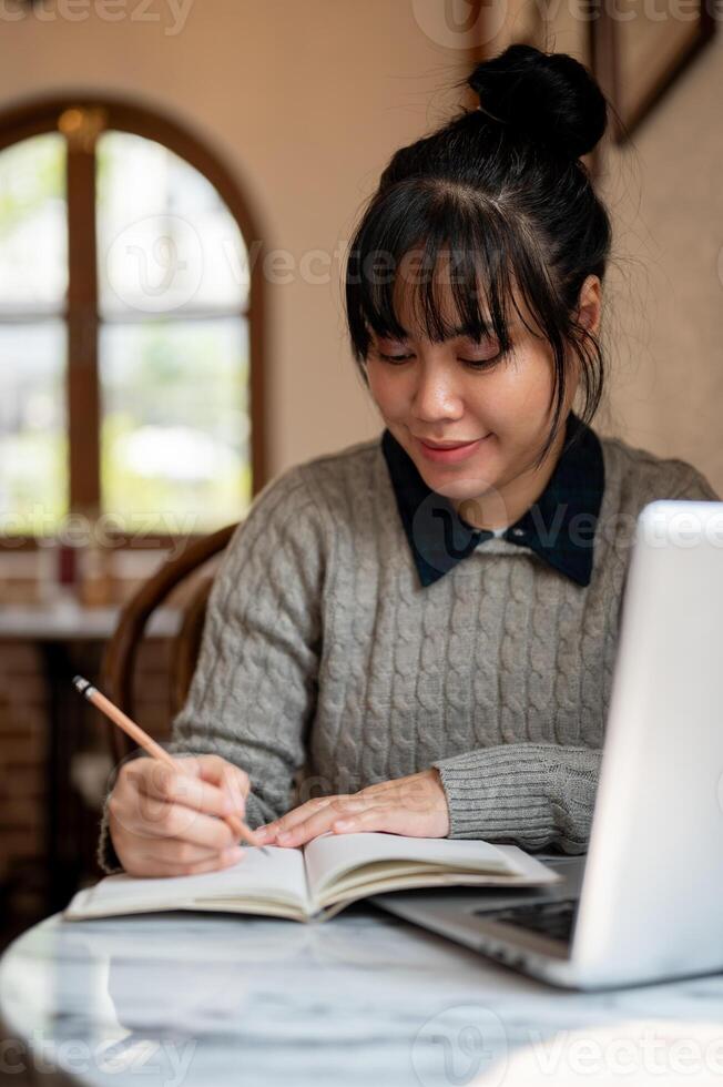 une femelle Université étudiant dans décontractée porter est en train de lire une cahier de texte ou Faire devoirs dans une café. photo