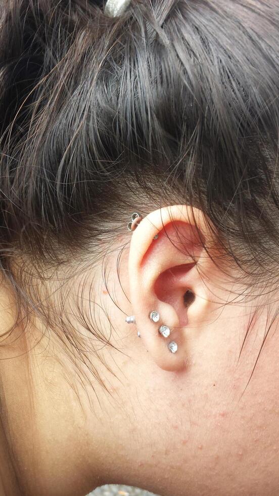 le oreille de une Jeune femme avec Trois des boucles d'oreilles sur le lobe et un sur le pavillon photo