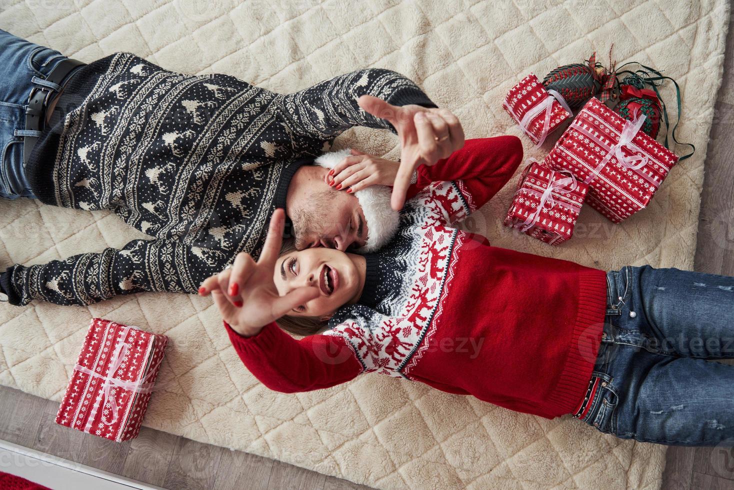 les mains en l'air. vue de dessus du couple en vêtements de noël se trouve sur le sol avec des cadeaux dessus photo