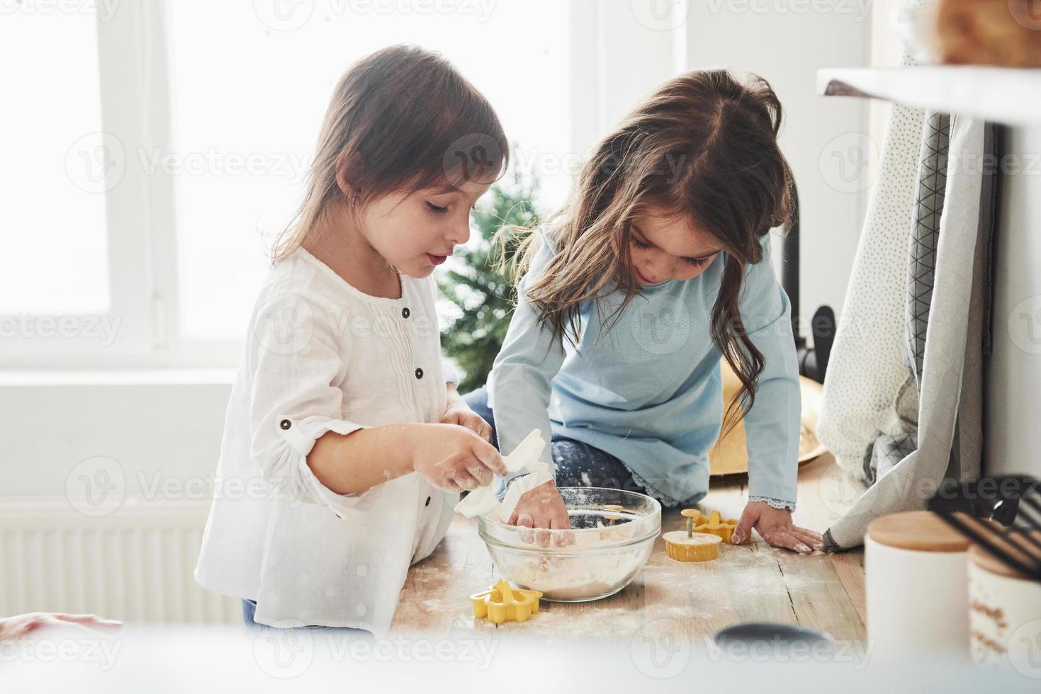 ceux-ci sont axés sur le travail. amis d'âge préscolaire apprenant à cuisiner avec de la farine dans la cuisine blanche photo