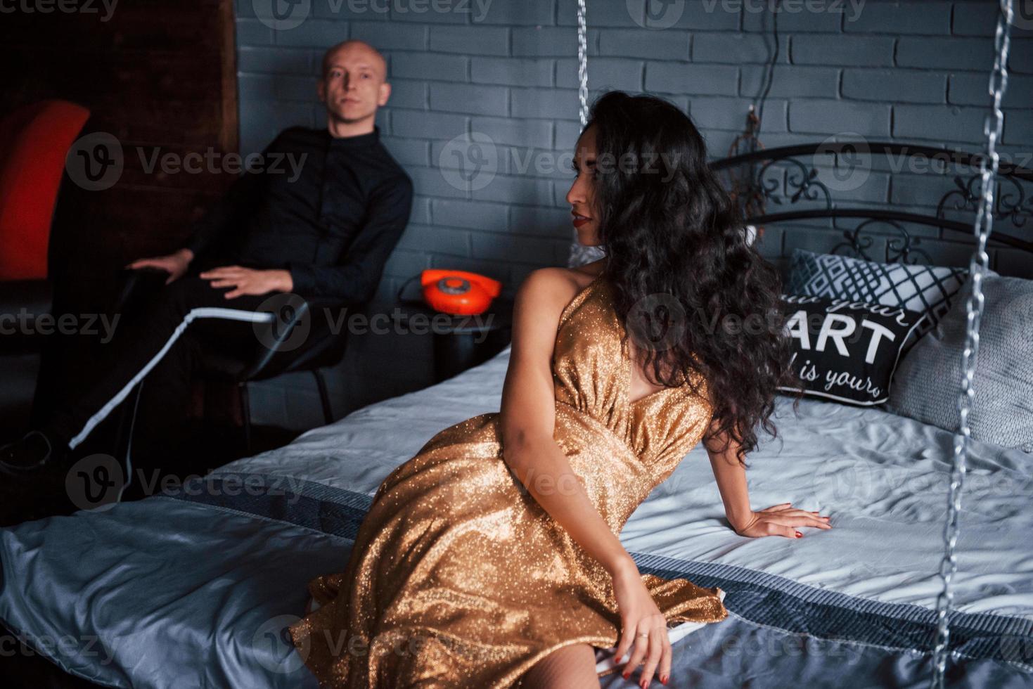 fille se tourna pour regarder son mari. un couple en tenue classique est assis devant le magnifique lit décoré de luxe photo