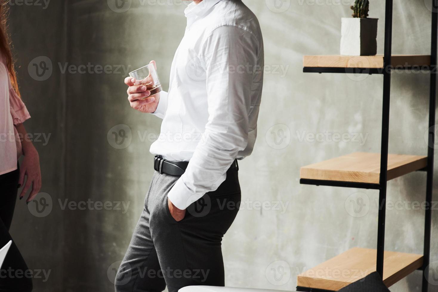 photo latérale d'un homme au bureau portant un verre avec de l'alcool. fille à gauche