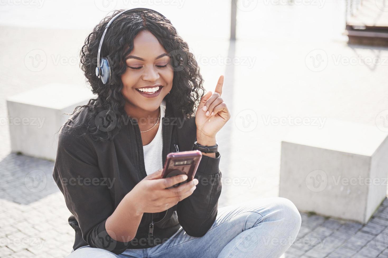 portrait d'une belle jeune jolie fille afro-américaine assise sur la plage ou le lac et écoutant de la musique dans ses écouteurs photo