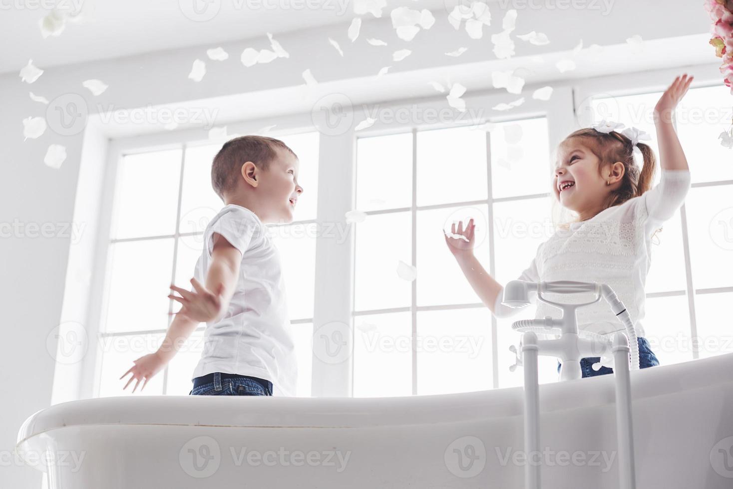 enfant jouant avec des pétales de rose dans la salle de bain à domicile. petite fille et garçon s'amusant et s'amusant ensemble. le concept de l'enfance et la réalisation des rêves, de la fantaisie, de l'imagination photo