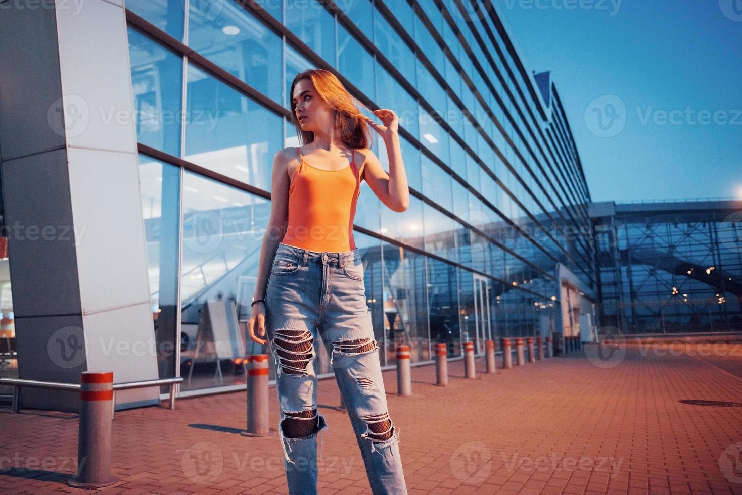 une belle jeune fille avec un sac à dos derrière ses épaules, debout dans la rue près d'un aéroport. elle vient d'arriver du reste et très contente photo