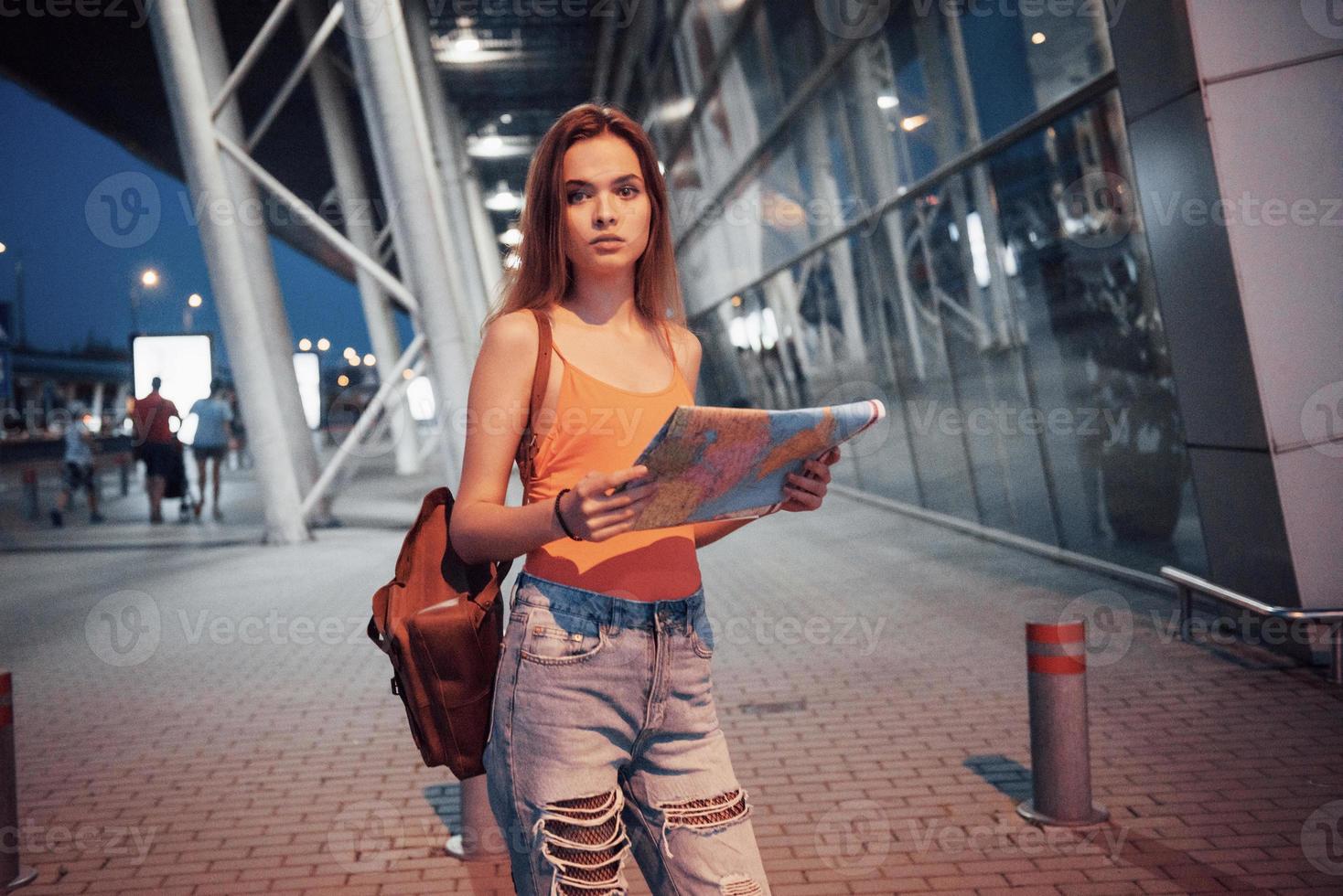 une belle jeune fille avec un sac à dos derrière ses épaules, debout dans la rue près d'un aéroport. elle vient d'arriver du reste et très contente photo