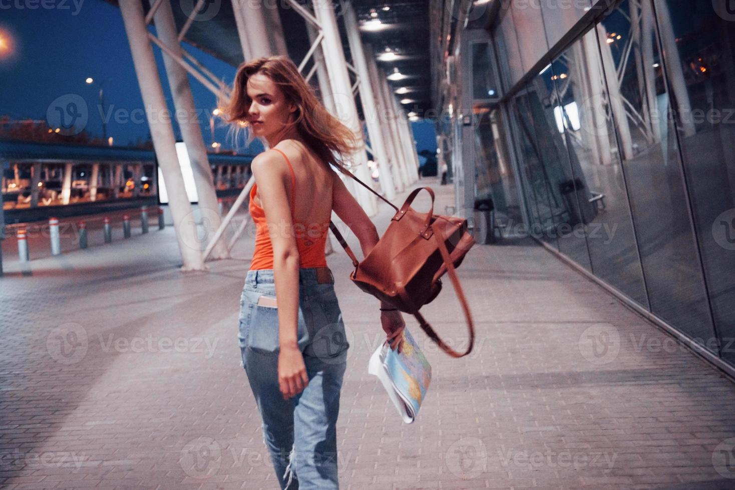 une belle jeune fille avec un sac à dos derrière ses épaules, debout dans la rue près d'un aéroport. elle vient d'arriver du reste et très contente photo