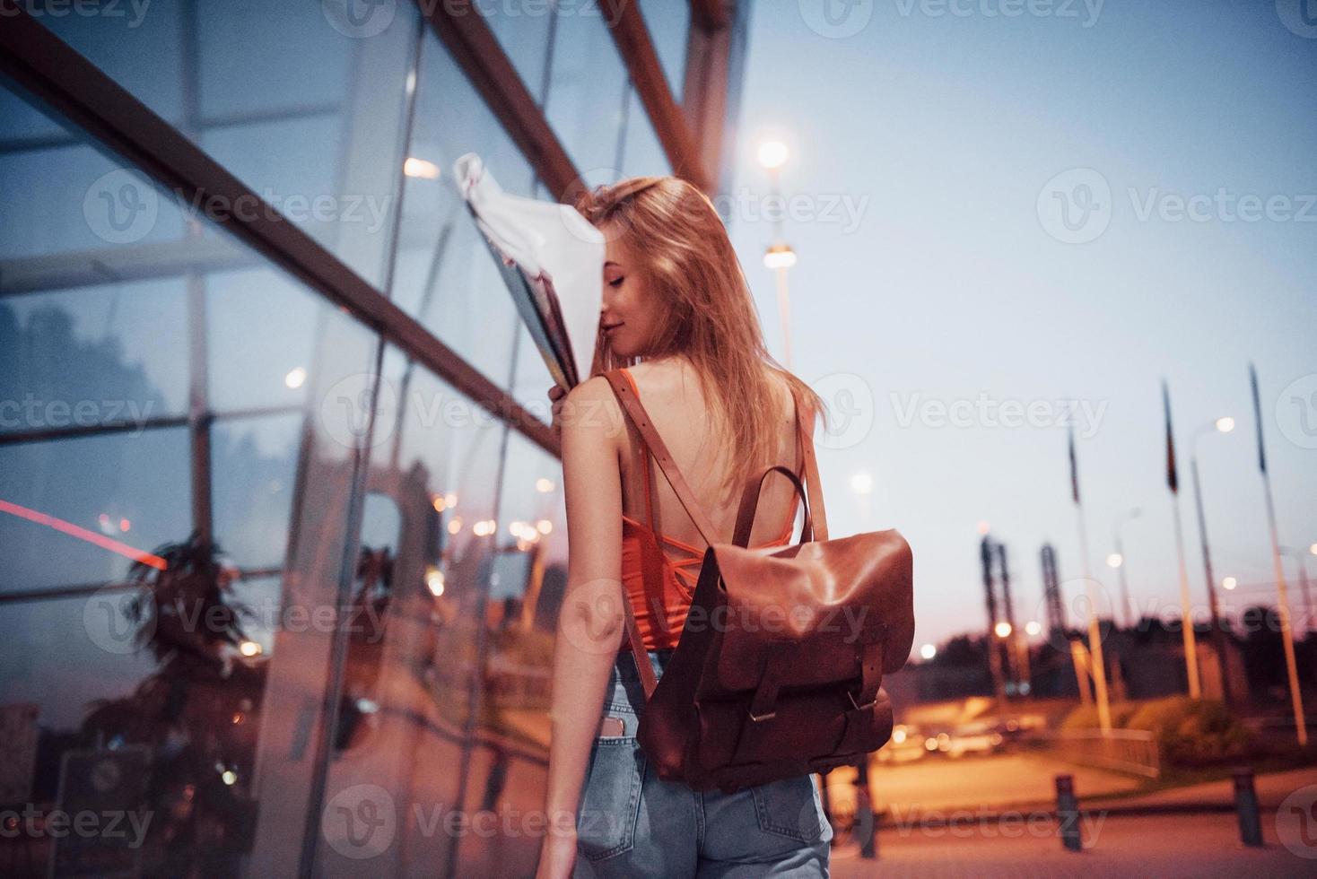 une belle jeune fille avec un sac à dos derrière ses épaules, debout dans la rue près d'un aéroport. elle vient d'arriver du reste et très contente photo