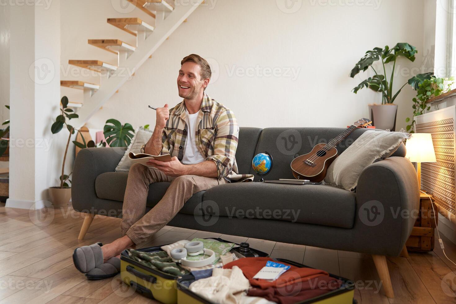 portrait de Jeune musicien, touristique des plans le sien suivant voyage, détient stylo et papier, crée vérifier liste de articles à prendre sur vacances, packs valise pour vacances photo