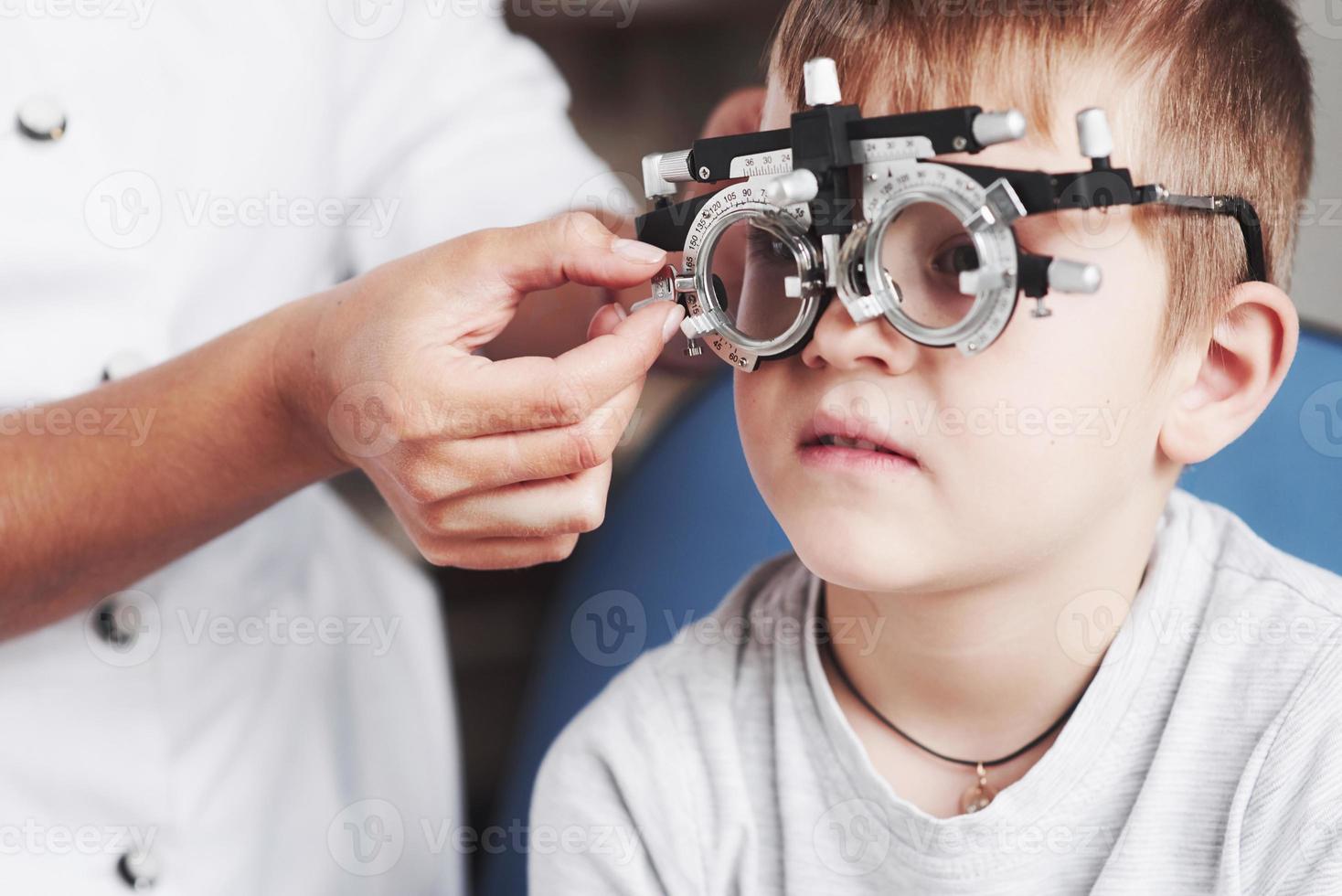 s'il te plaît, concentre-toi. enfant assis dans le cabinet du médecin et ont testé son acuité visuelle photo