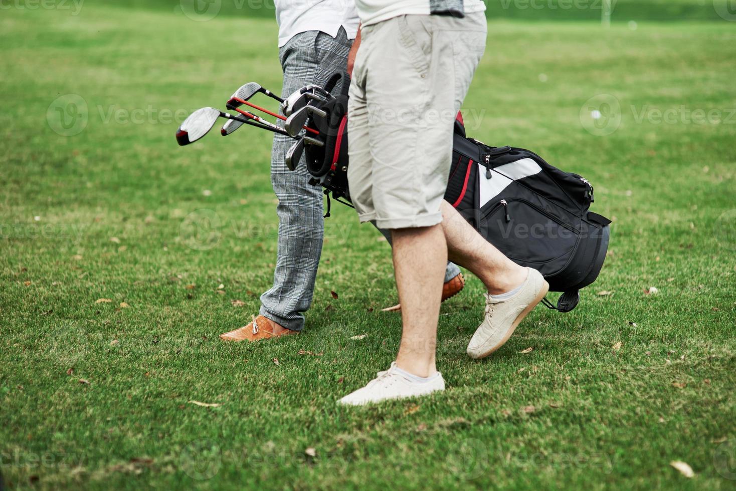 marcher jusqu'à la destination. photo recadrée de deux amis sur le terrain de sport avec équipement de golf