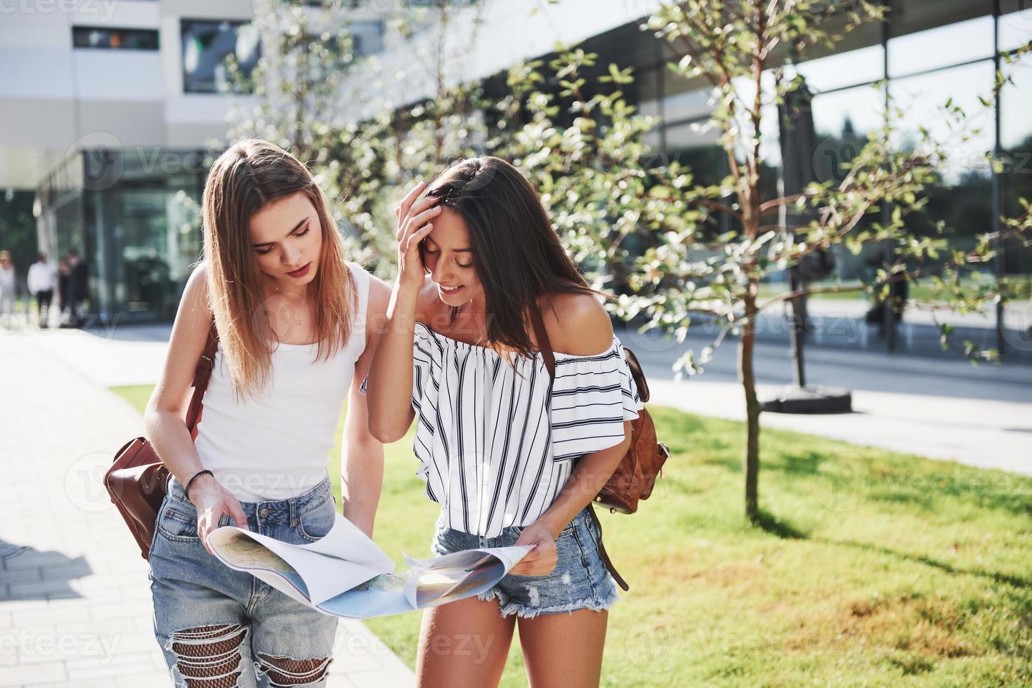 jeunes filles lisant le plan de la ville et cherchant un hôtel. de beaux touristes avec des sacs à dos déterminent le concept de connaissance du monde photo