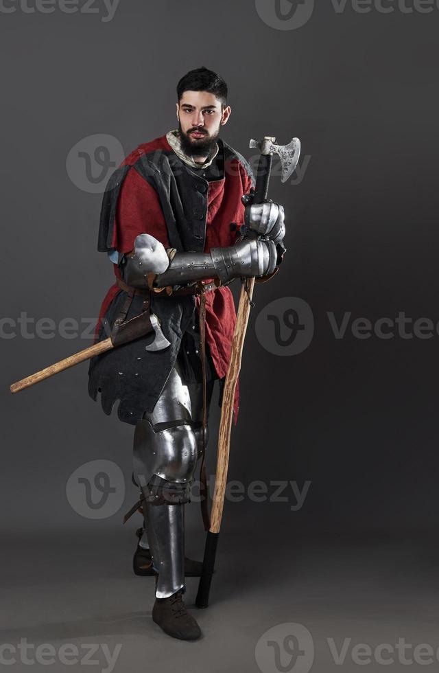 chevalier médiéval sur fond gris. portrait d'un guerrier brutal au visage sale avec une armure de cotte de mailles, des vêtements rouges et noirs et une hache de combat photo