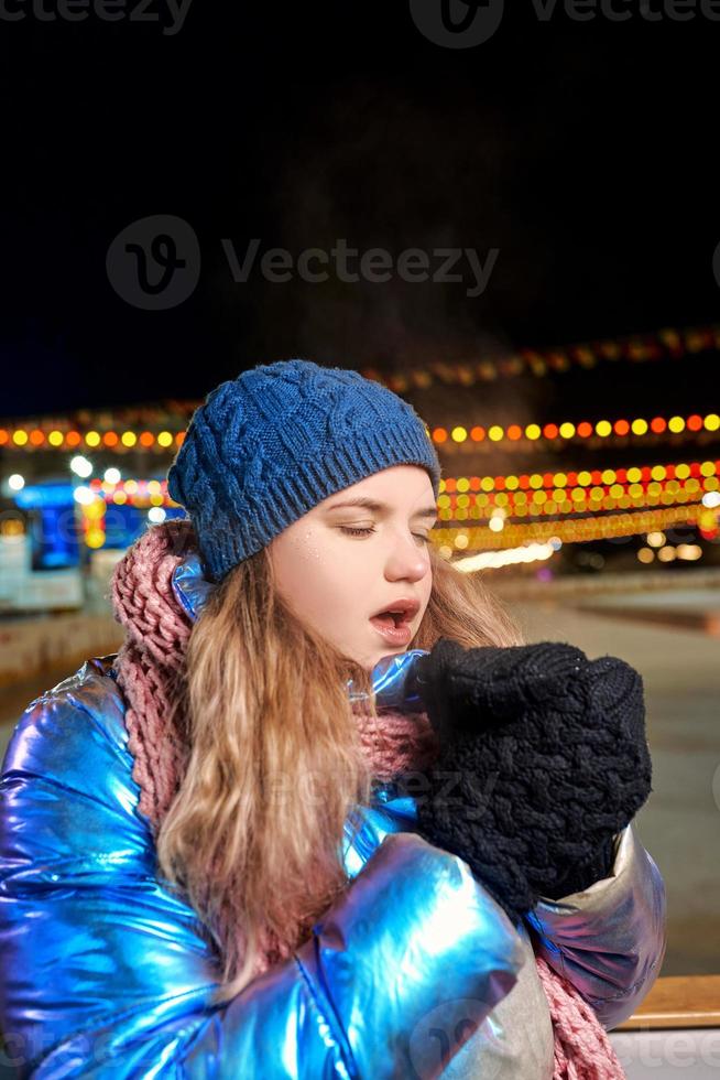 heureuse jeune femme caucasienne souriante en écharpe, chapeau, veste, mitaines près de la patinoire extérieure. nouvel an, amusement, concept d'hiver photo