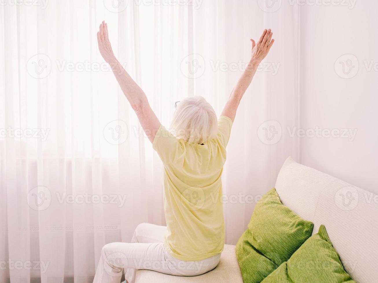 femme élégante caucasienne joyeuse aux cheveux gris assis sur le canapé à la maison. anti-âge, mode de vie sain, concept de pensée positive photo