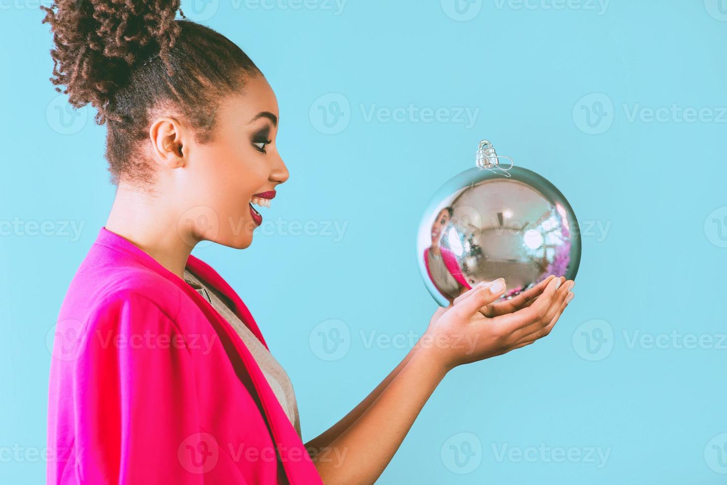 joyeuse femme afro-américaine tenant dans ses mains une décoration de boule de noël. noël, nouvel an, bonheur, concept de vacances photo