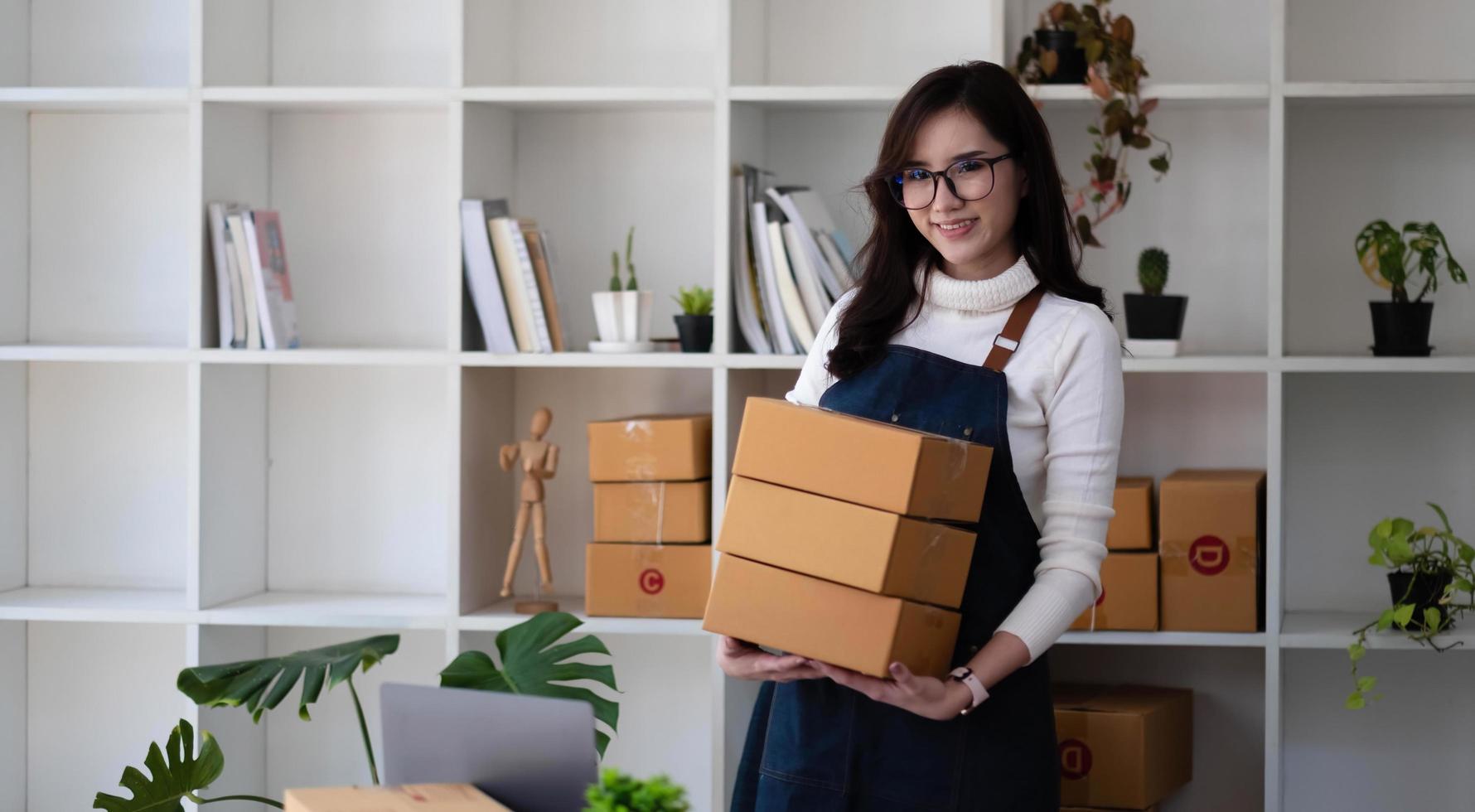 portrait d'une jeune femme asiatique sme travaillant avec une boîte à la maison le lieu de travail. propriétaire de petite entreprise de démarrage, entrepreneur de petite entreprise sme ou entreprise indépendante en ligne et concept de livraison. photo