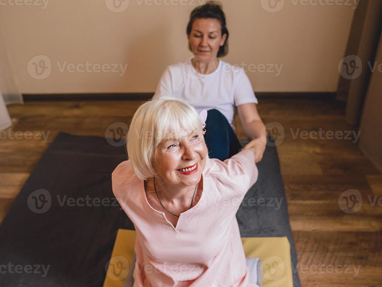 femme élégante caucasienne senior aux cheveux gris et phalaenopsis rose dans ses cheveux assis au massage thaï. anti-âge, mode de vie sain, voyage, concept de massage thaï photo