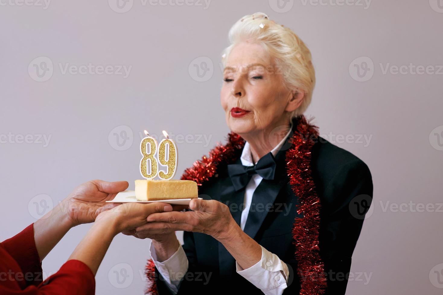 Heureuse femme de quatre-vingt-neuf ans élégante et joyeuse en costume noir célébrant son anniversaire avec un gâteau. mode de vie, positif, mode, concept de style photo