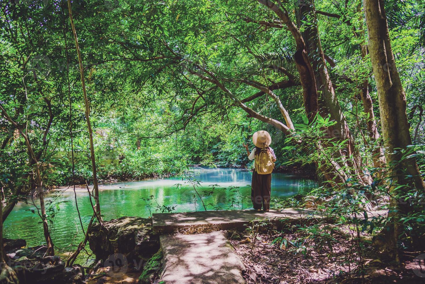 fille avec un sac à dos jaune marche nature de voyage. voyageur hipster élégant marchant dans la forêt tropicale ensoleillée. beaux ruisseaux émeraude et arbres verts dans la forêt tropicale. tourisme, randonnée photo
