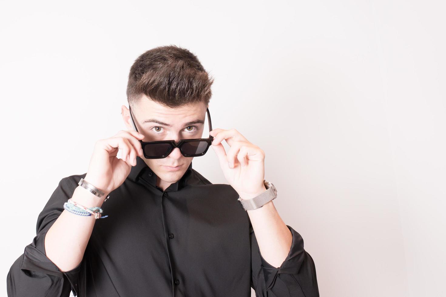 prise de vue en studio d'un jeune homme séduisant en noir portant des lunettes de soleil. fond blanc. photo