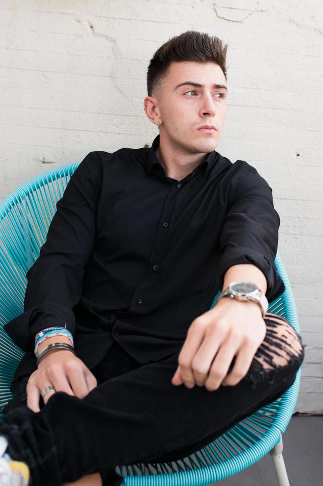jeune homme sur une terrasse, assis sur une chaise bleue moderne. en noir photo