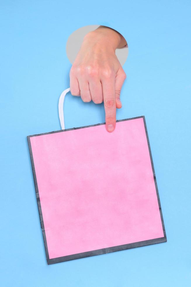 main féminine tenant un sac en papier rose sur fond bleu photo