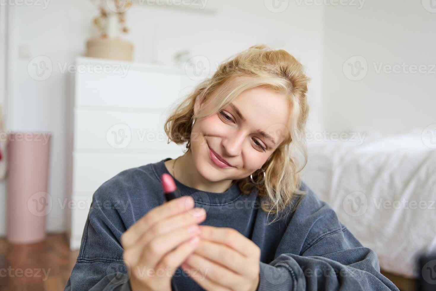 portrait de souriant magnifique femme dans sa chambre, séance et montrant rouge à lèvres, recommander préféré beauté produit, contenu fabricant enregistrement une de se pour social médias Blog photo