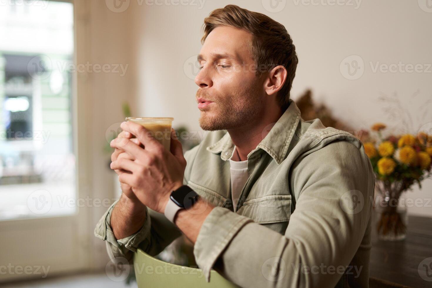 portrait de Jeune Beau barbu homme dans café boutique, séance sur chaise, sirotant cappuccino, repos dans café photo