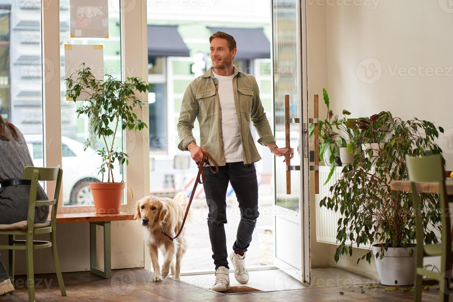 portrait de Beau souriant Jeune homme, en marchant dans le café magasin avec le sien mignonne chien, d'or retriever sur laisse. gars entre dans acceptant les animaux café photo