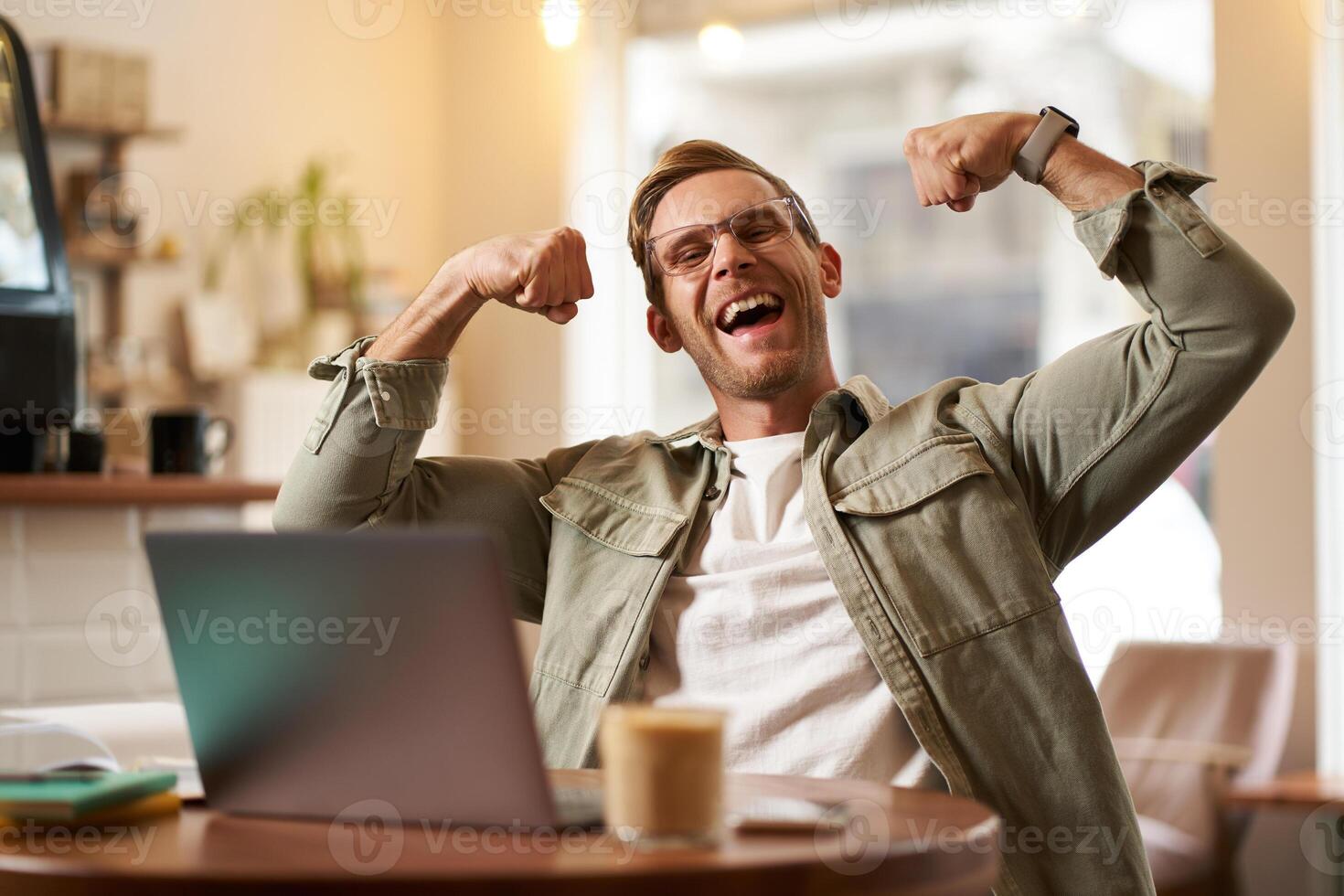 portrait de beau, heureux Jeune homme spectacles biceps, fléchissement muscles, est assis dans de face de portable dans café, réjouissance, privé entraîneur ayant une bavarder avec le sien client photo