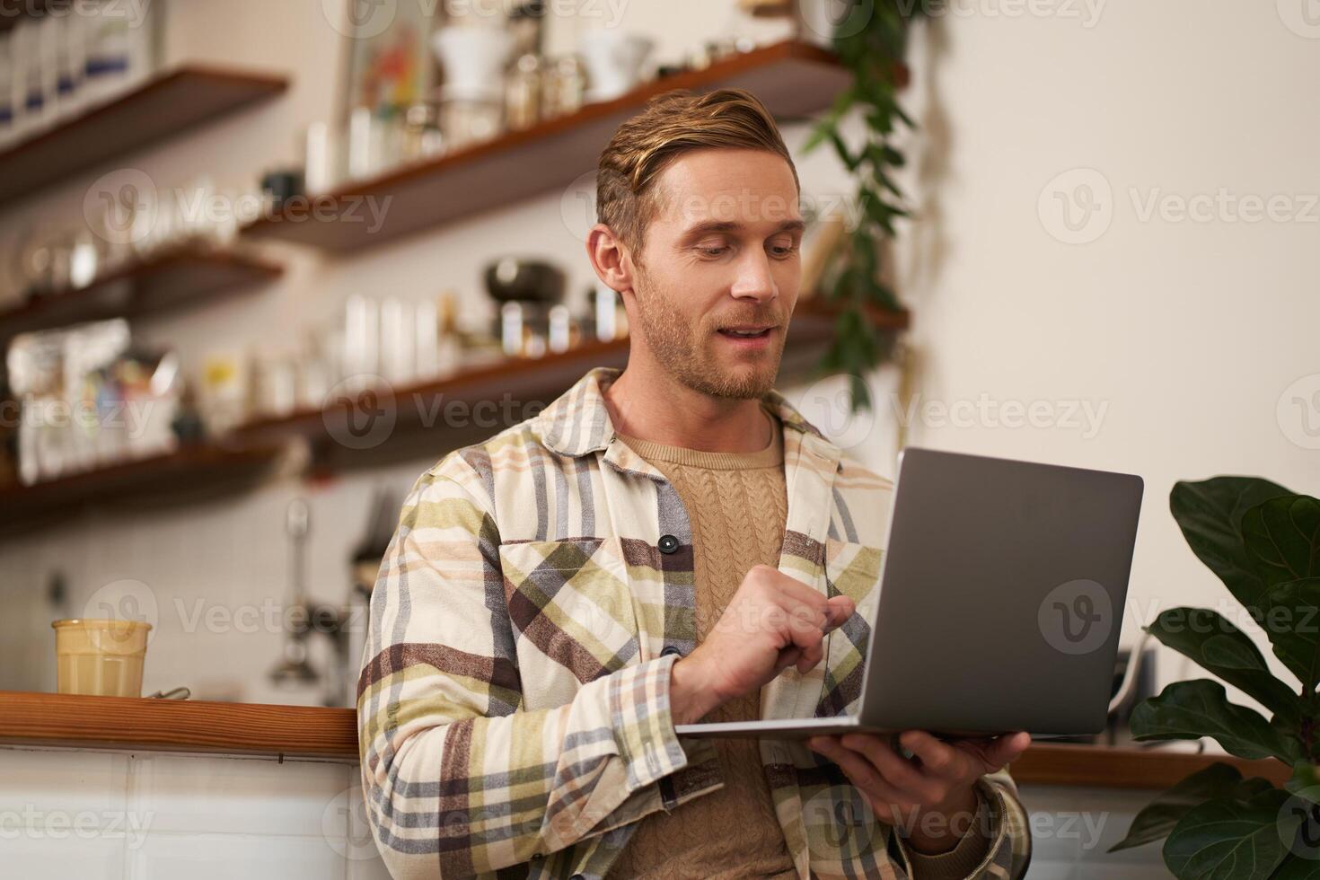 portrait de Beau Jeune homme avec ordinateur portable, séance dans café, à la recherche à filtrer, Faire travail tâche, travail comme une pigiste, a éloigné espace de travail photo