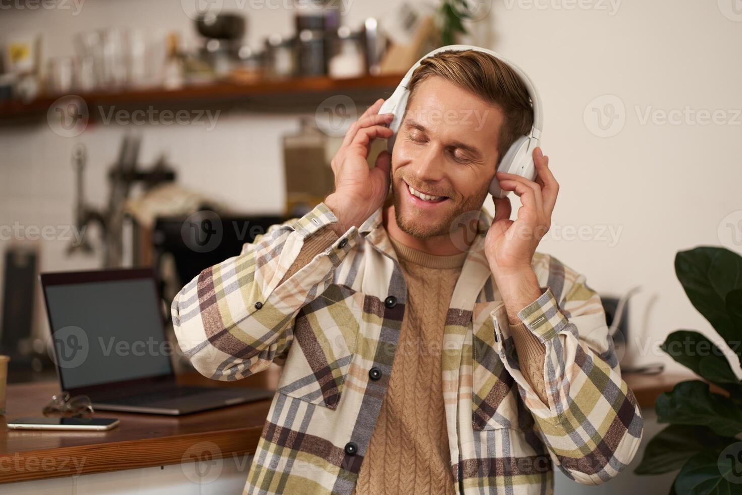 portrait de Jeune homme séance avec portable dans café, écoute la musique dans écouteurs, souriant avec yeux fermé, heureux par le du son qualité photo