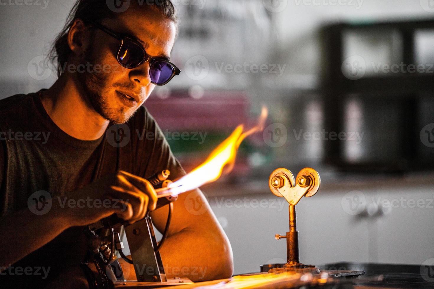 jeune homme de soufflage de verre travaillant sur une flamme de torche avec des tubes de verre photo