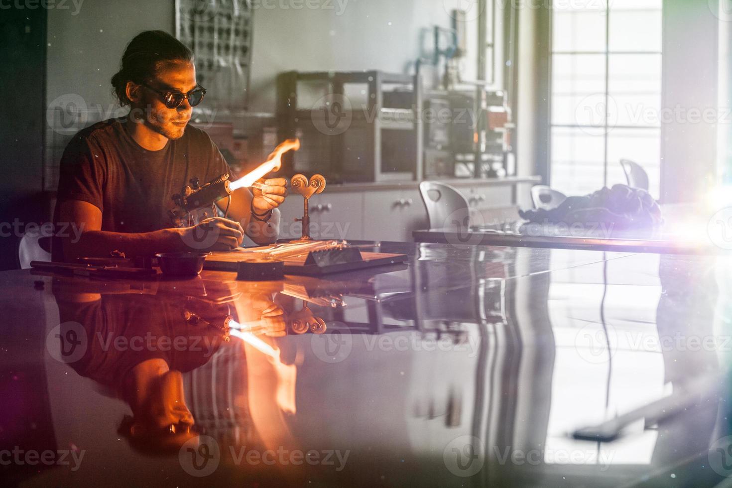 jeune homme de soufflage de verre travaillant sur une flamme de torche avec des tubes de verre photo